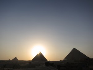 The sun setting behind the Pyramid of Khafre, with the Great Pyramid of Giza on the right and the Pyramid of Menkaure on the left