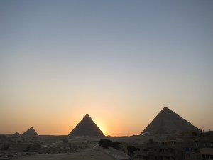 The sun setting behind the Pyramid of Khafre, with the Great Pyramid of Giza on the right and the Pyramid of Menkaure on the left